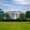 far shot of the back of The White House showing green lawn and blue sky