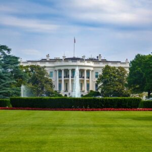far shot of the back of The White House showing green lawn and blue sky