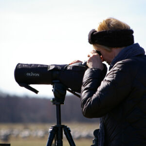 Person outdoors in coat using binoculars that are on a tripod