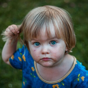 closeup on head of toddler who is holding out some the hair on her head with one hand