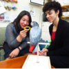 two women interact with African grey parrot